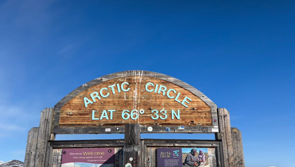 Sign indicating Arctic Circle latitude against a clear blue sky.