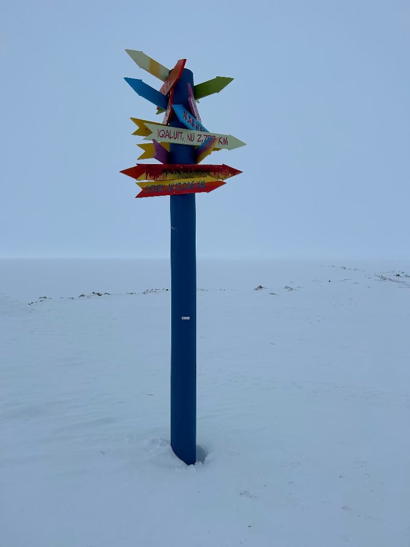 Colorful signpost in the snow against a clear blue sky, on the road to Inuvit and Arctic Ocean Canada.