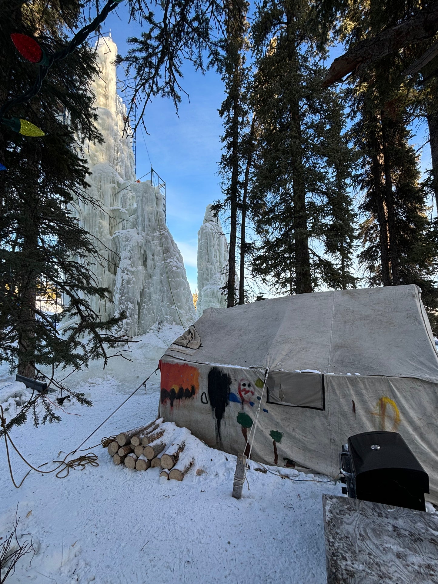 The stunning ice tower at Mount Sima stands tall, framed by the cozy wall tent set up for a delicious fondue meal. After an exhilarating day of ice climbing, adventurers relax by the warmth of the fire, enjoying a comforting meal in the heart of the Yukon’s frozen landscape.