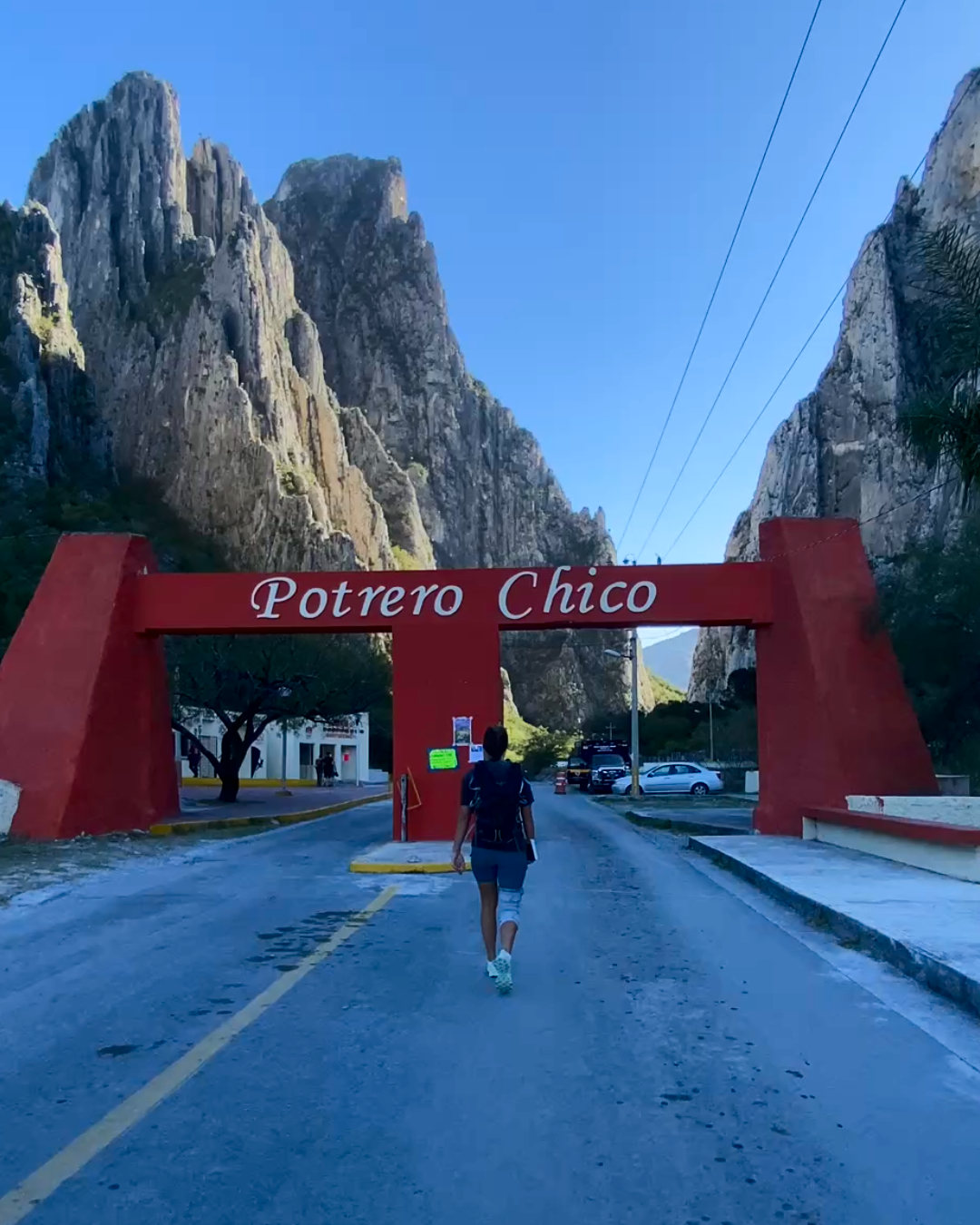 Person walking under a red 'Potrero Chico' archway with mountains in the background
