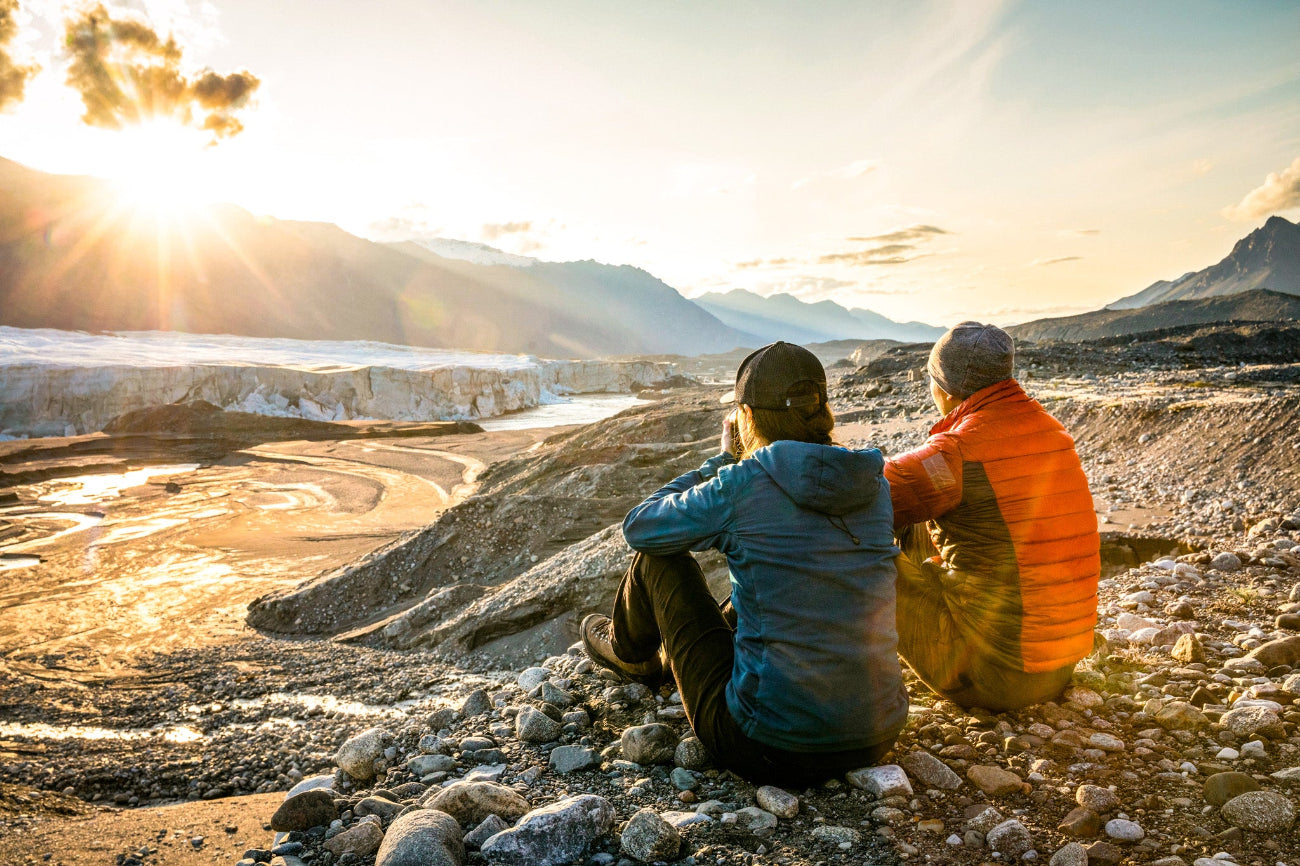 A group of adventurers seated in awe, taking in the breathtaking view of the Donjek Glacier. Surrounded by towering ice and rugged mountain landscapes, they pause to appreciate the raw beauty and vastness of the Yukon wilderness.