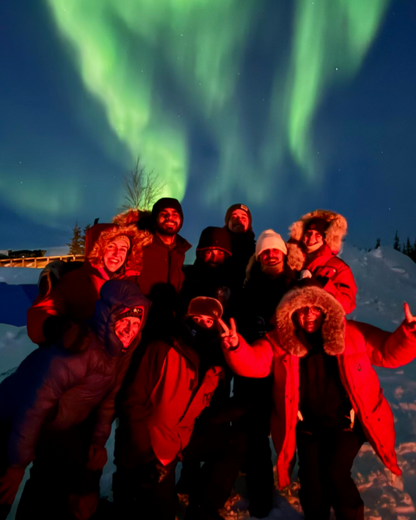 Group of people posing in front of a stunning display of the Northern Lights.