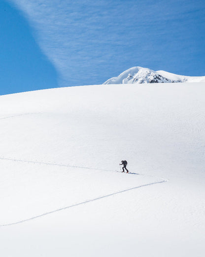 Person skiing alone on a snowy mountain with a clear blue sky