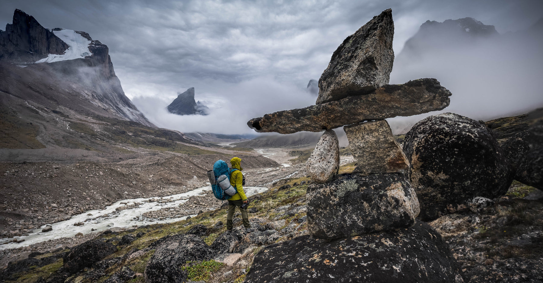 Hiker with a backpack walking through a mountainous landscape with stone cairns.