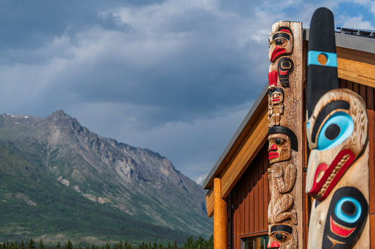Wooden totem poles with colorful carvings in front of a mountainous landscape