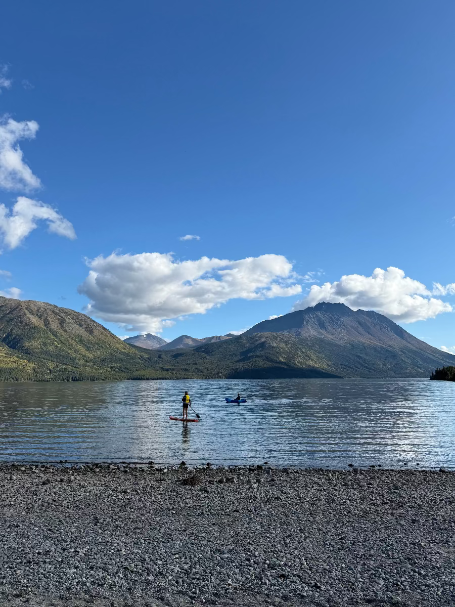 Person paddleboarding on a lake with mountains in the background Carcross area Yukon