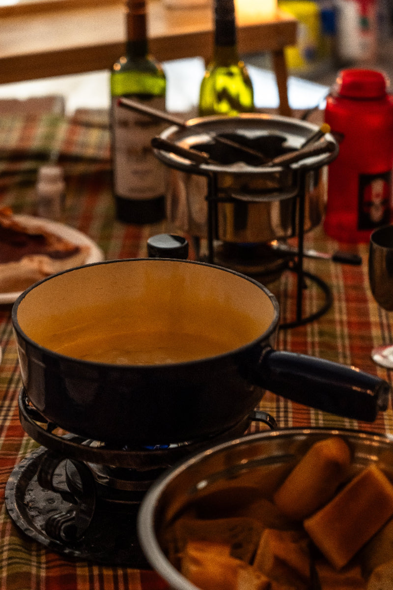 Fondue setup with pots, wine bottles, and bread on a table.