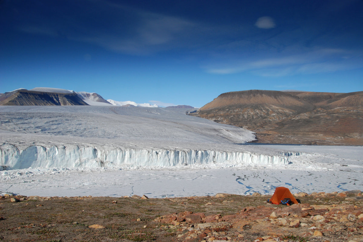 Glacier with a person in an orange jacket standing on a rocky foreground