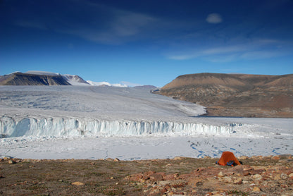 Glacier with a person in an orange jacket standing on a rocky foreground