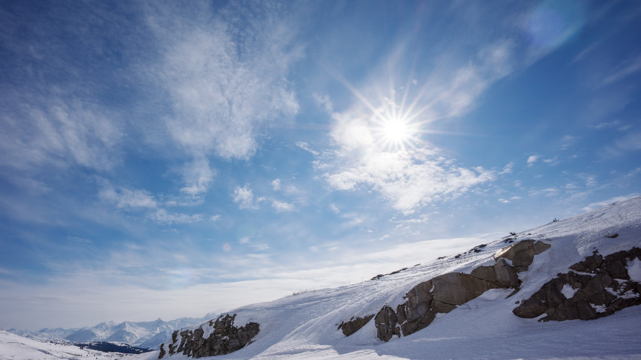 Snowy mountain landscape with a clear blue sky and sun.