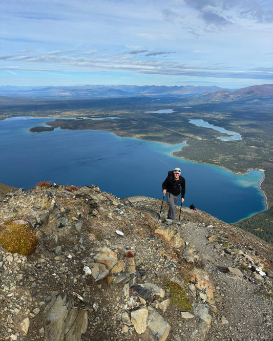 Person hiking on a mountain top with a scenic view of lakes and mountains.