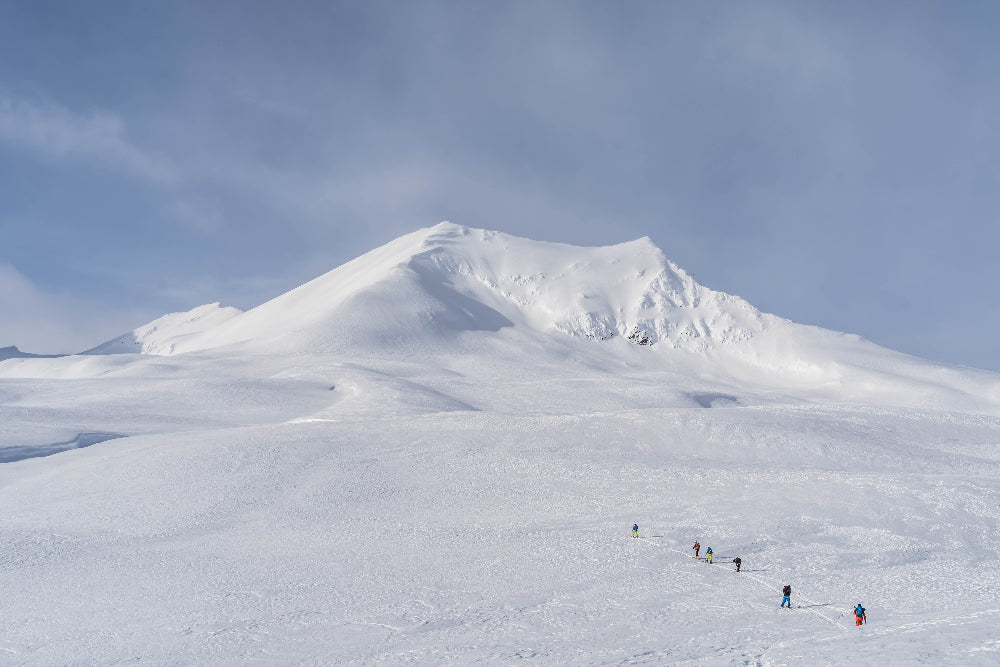 Group of people skiing, skinning up on a snow-covered mountain with a large peak in the background, Yukon Canada