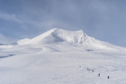 Group of people skiing, skinning up on a snow-covered mountain with a large peak in the background, Yukon Canada
