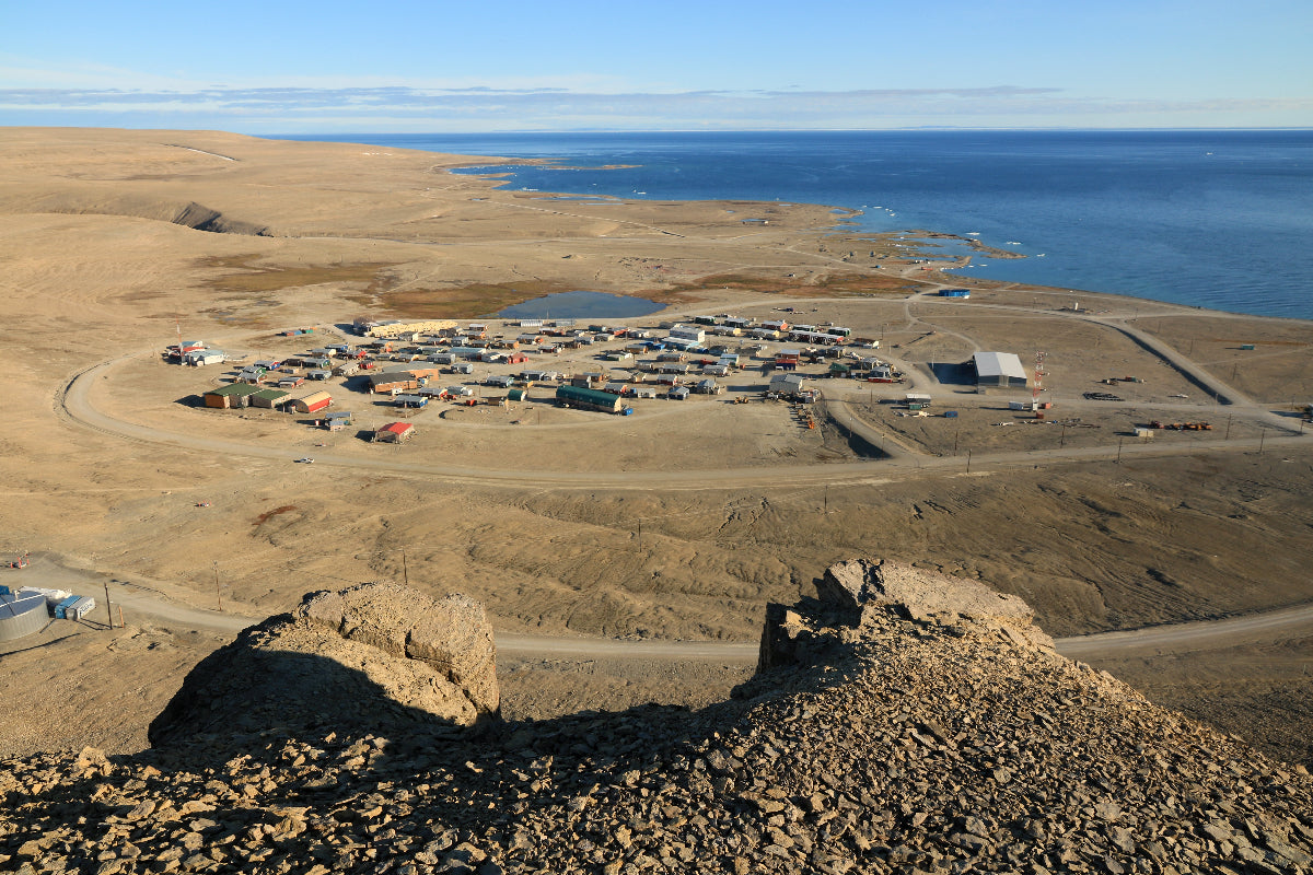Remote coastal settlement with buildings and infrastructure, surrounded by rocky terrain and ocean.