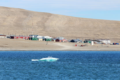 Small town by a body of water with an iceberg floating nearby