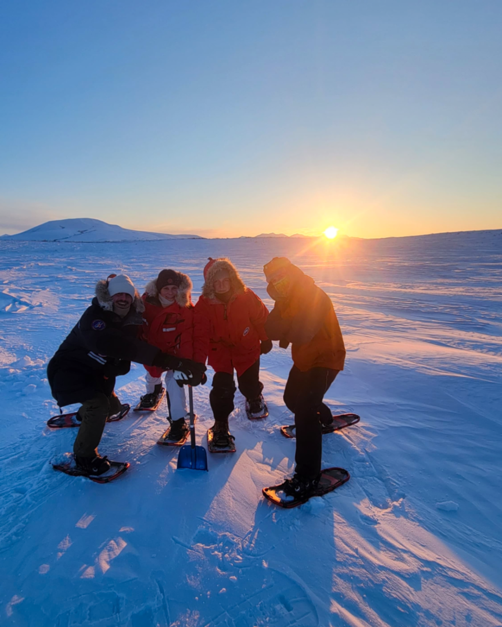 Four people snowshoeing in a snowy landscape with a sunset in the background