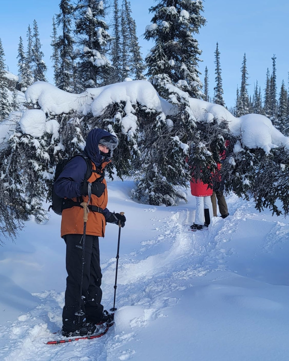 Two people snowshoeing through a snowy forest with trees covered in snow.
