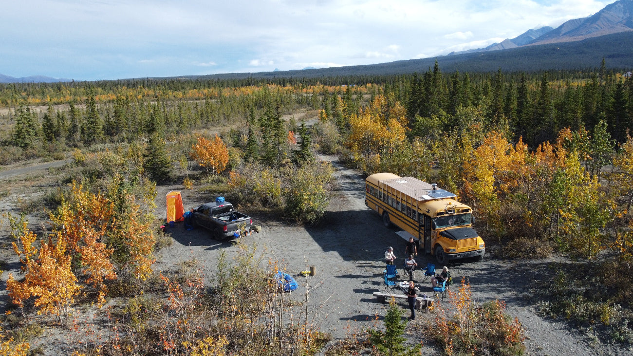 Yellow school bus parked in a remote area with trees and mountains in the background