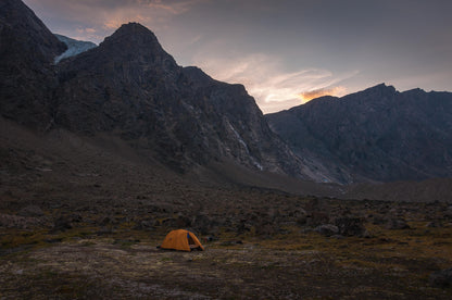Orange tent in a mountainous landscape with a sunset, Summit Valley Akshayuk Pass, Auyuittuq National Park