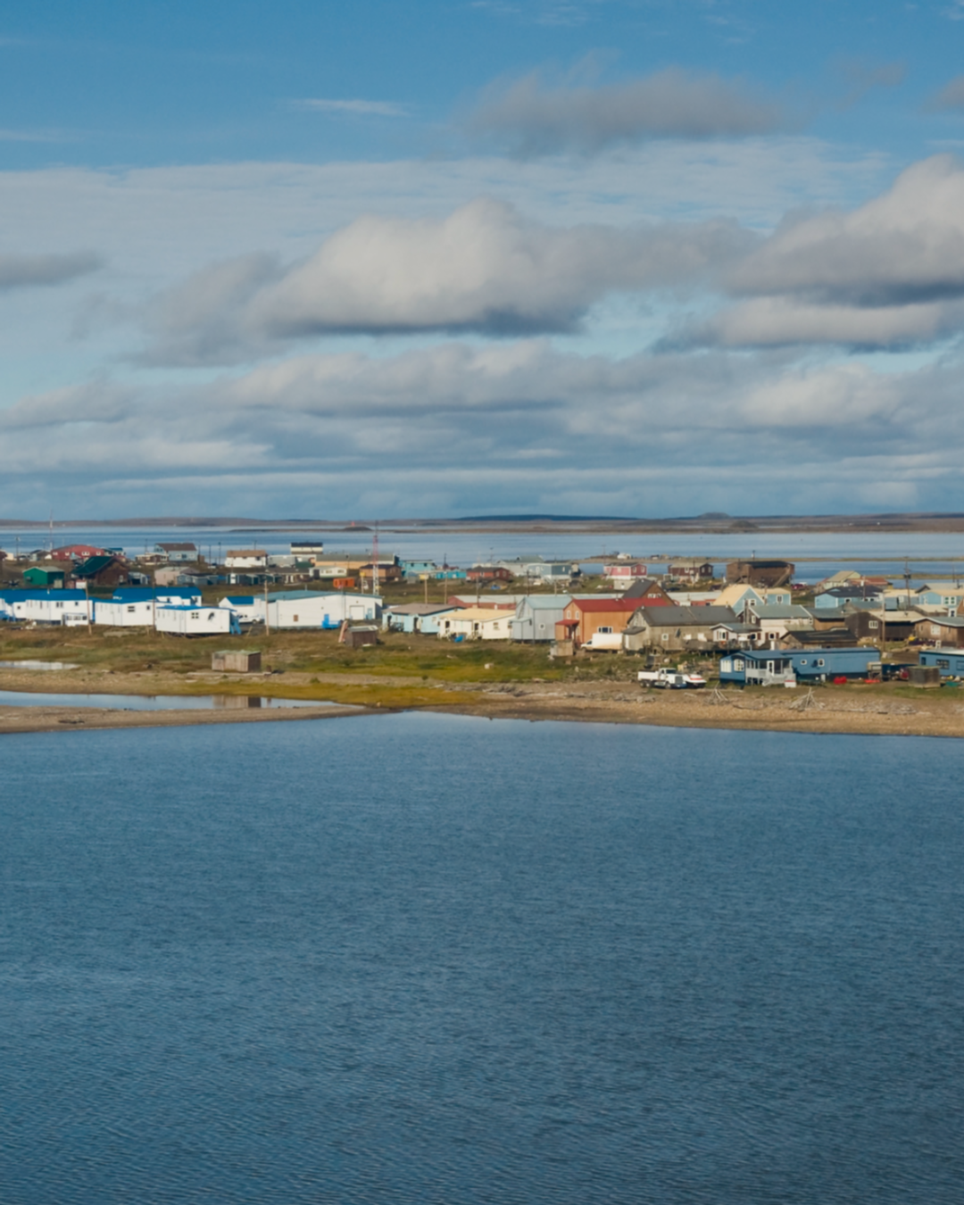 Small town of Tuktoyaktuk in North West Territories in the Arctic by a body of water with a blue sky and clouds.