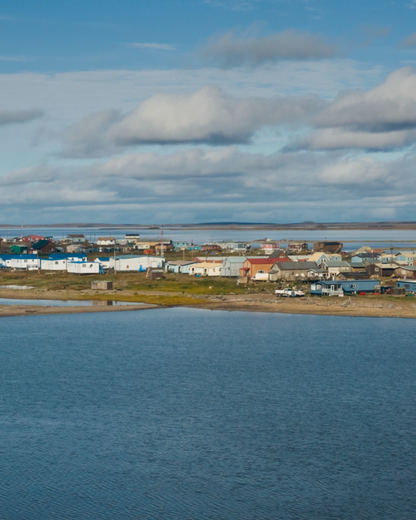 Small town of Tuktoyaktuk in North West Territories in the Arctic by a body of water with a blue sky and clouds.