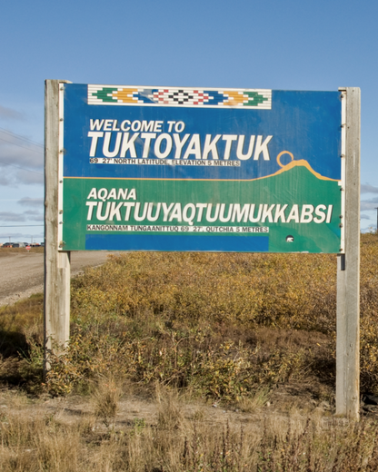 Welcome sign to Tuktoyaktuk with blue and green colors, featuring text and patterns.